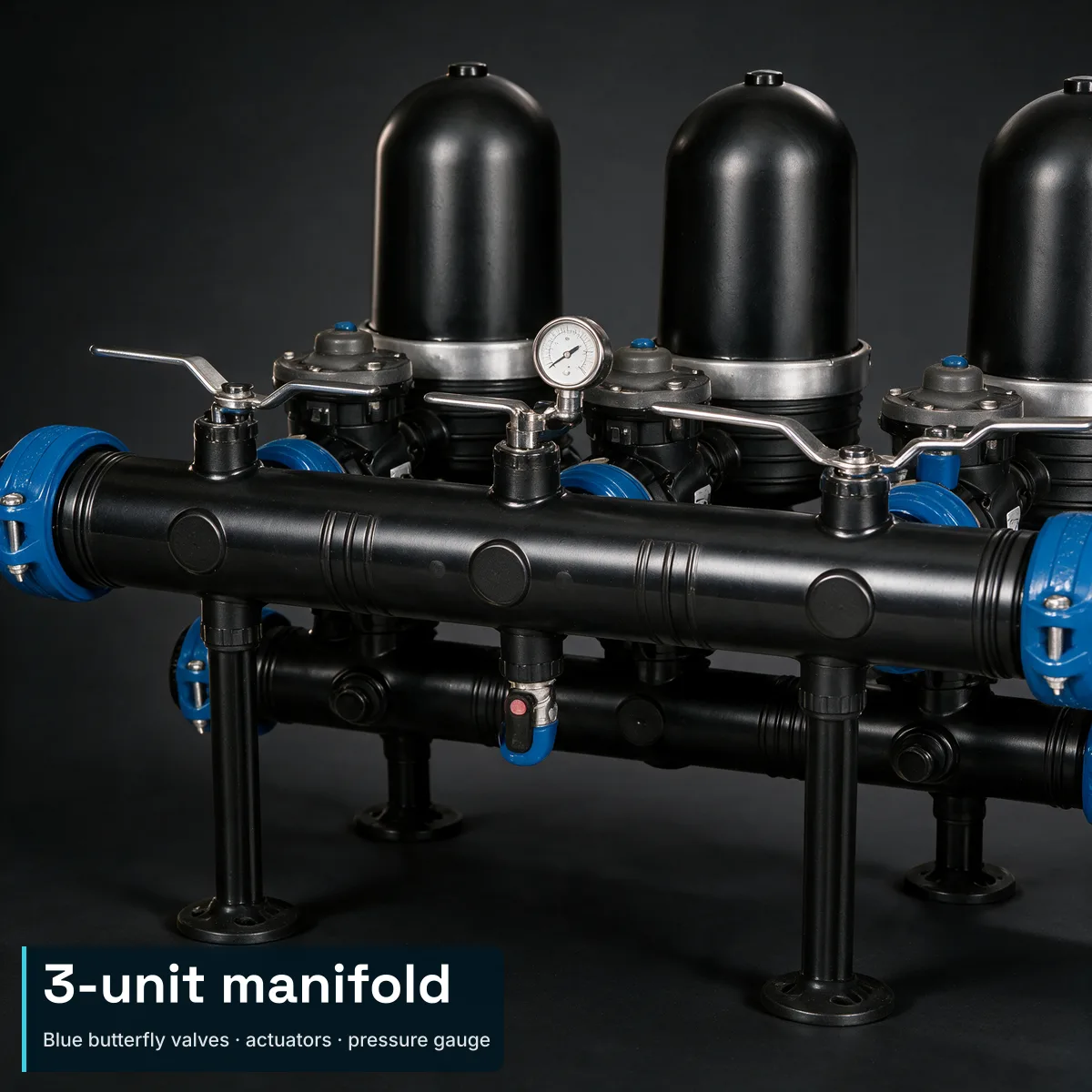 Close-up of three ARKAL by Amiad 2" Spin Klin industrial units manifolded together on a black horizontal header pipe — blue butterfly valves at the manifold ends, actuators at each unit base, pressure gauge on the manifold. A compact editorial text block anchored to the bottom-left over the leg/support area carries the integrated headline 3-unit manifold and the subtitle Blue butterfly valves · actuators · pressure gauge.