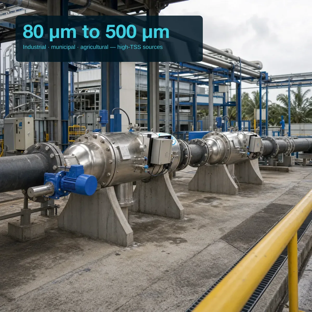 Wide-angle scenario view of one or two Filtersafe Trident E units on separate saddle supports in a Singapore or Malaysian large industrial water plant — polished SS horizontal bodies with blue gearmotors connected to large-bore flanged carbon-steel pipework; concrete structures, pipe bridges, and tropical humid atmosphere in background; editorial overlay top-left reads '80 μm to 500 μm' and 'Industrial · municipal · agricultural — high-TSS sources'.